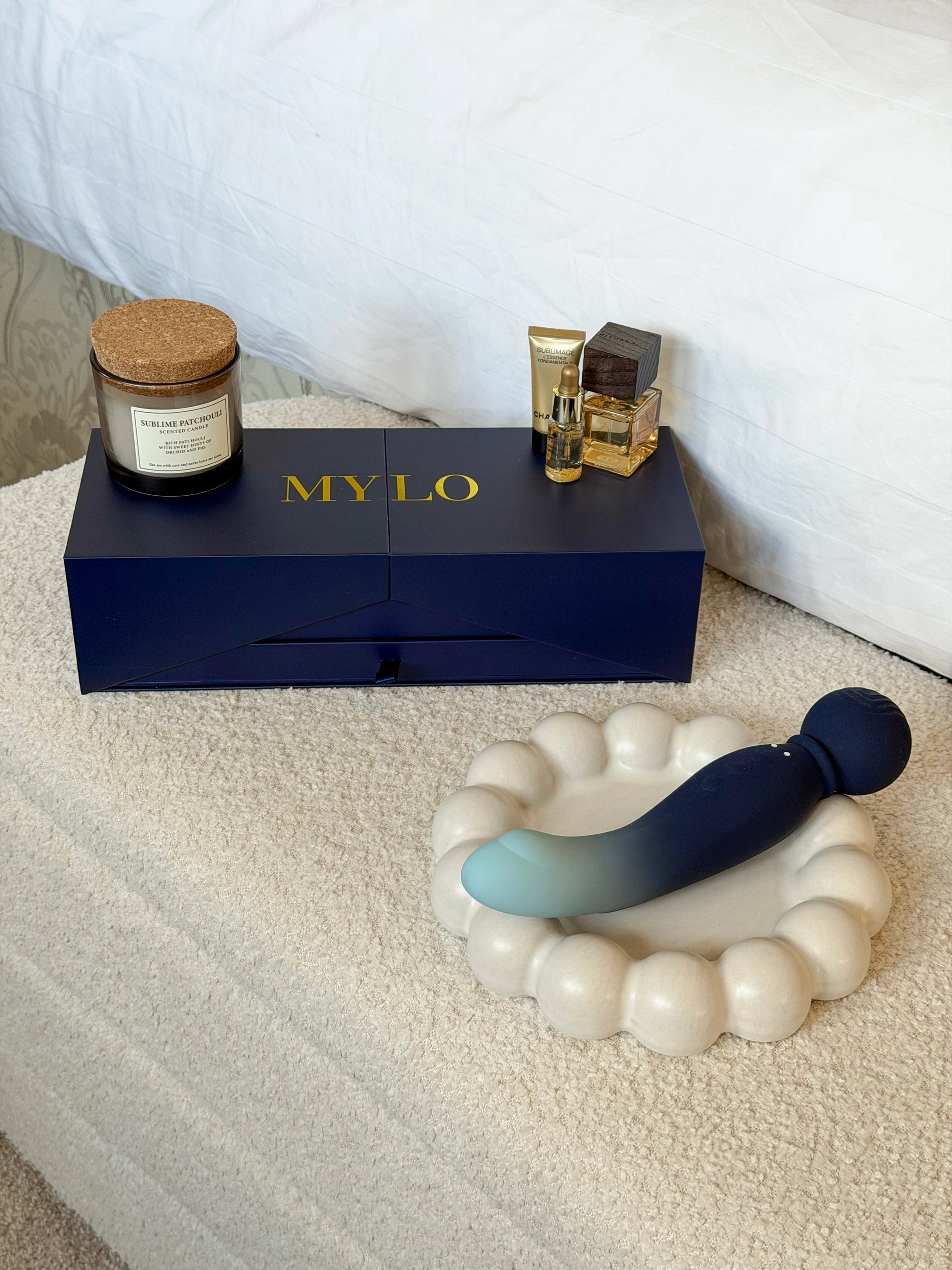 A sleek, gradient blue-to-navy silicone vibrator with a rounded head rests on an off-white ceramic dish.