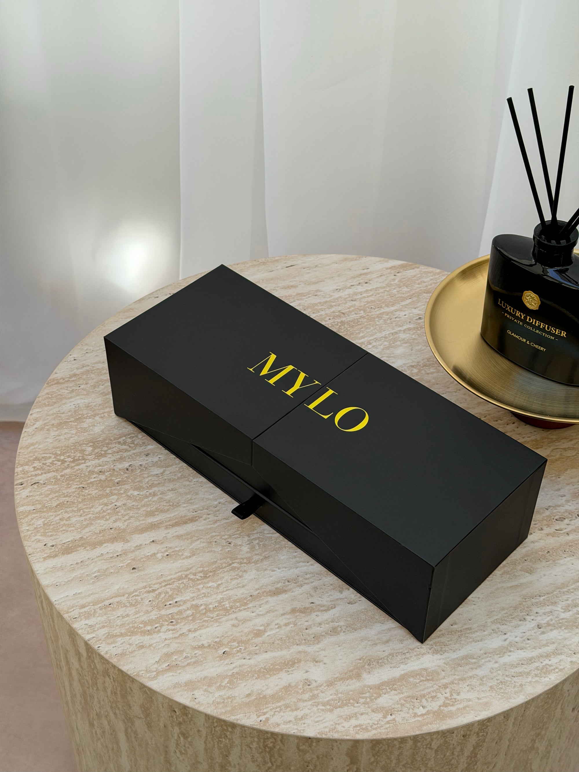 Black rectangular mylo brand box with gold lettering and a small black pull-tab on the front.