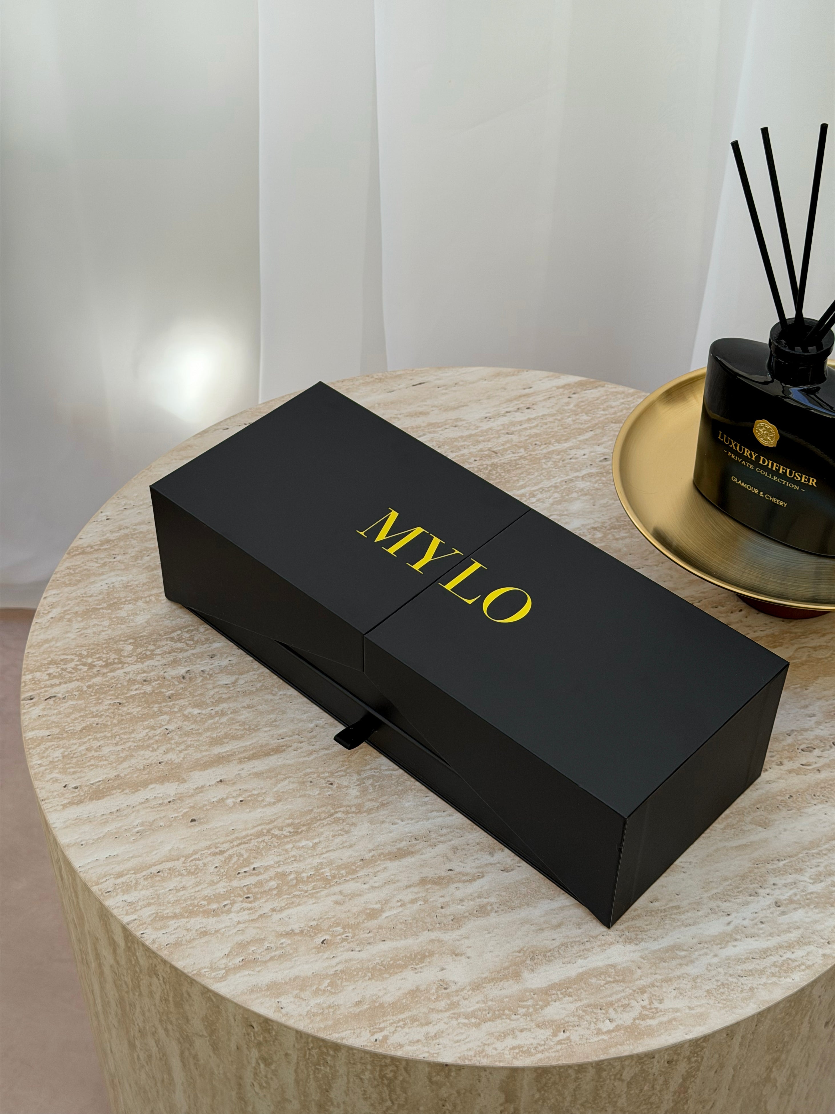 Black rectangular mylo brand box with gold lettering and a small black pull-tab on the front.