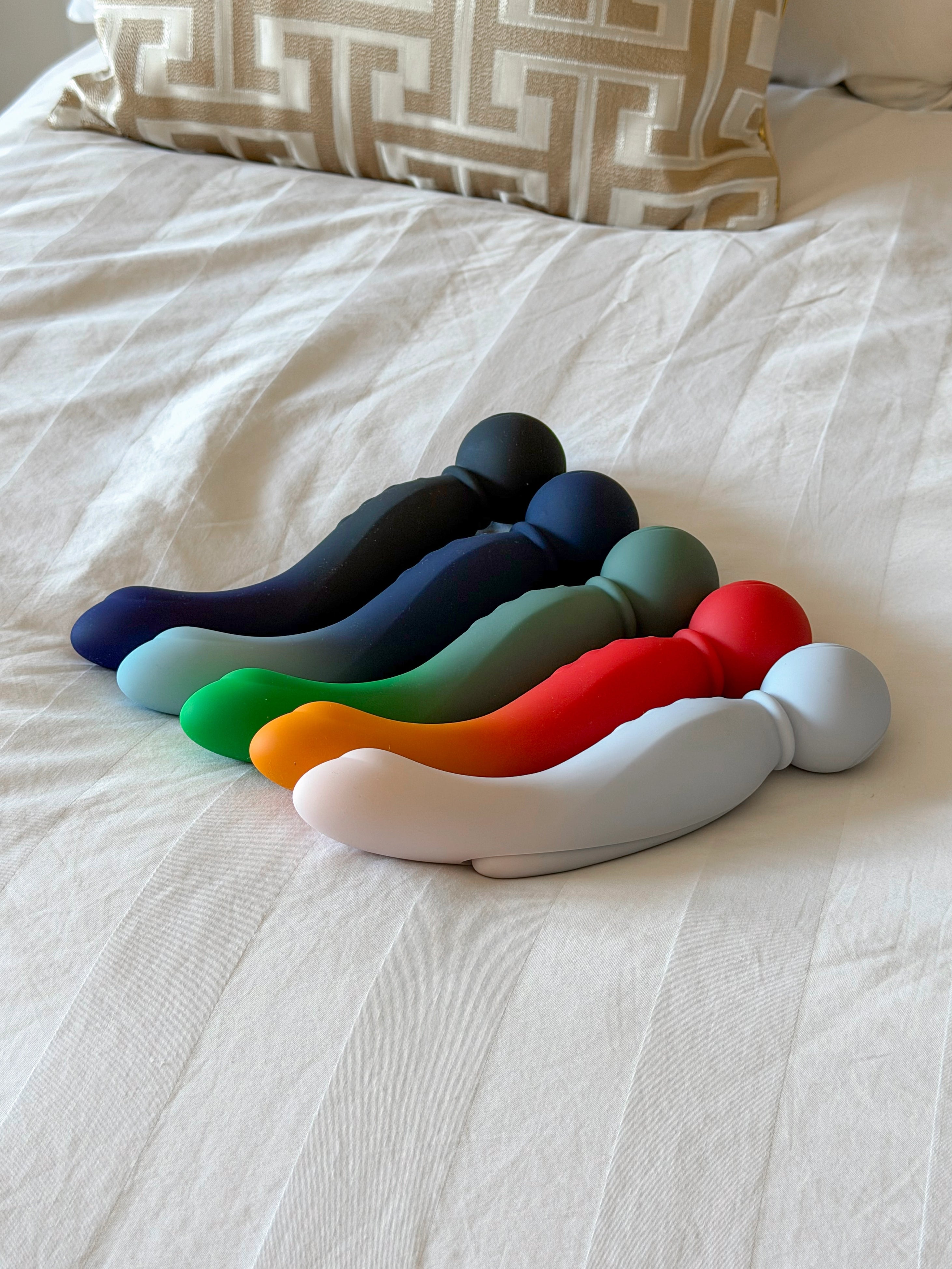 A set of six smooth, matte-finished silicone vibrators in assorted colors including black, navy blue, teal, green, red, orange, and white.