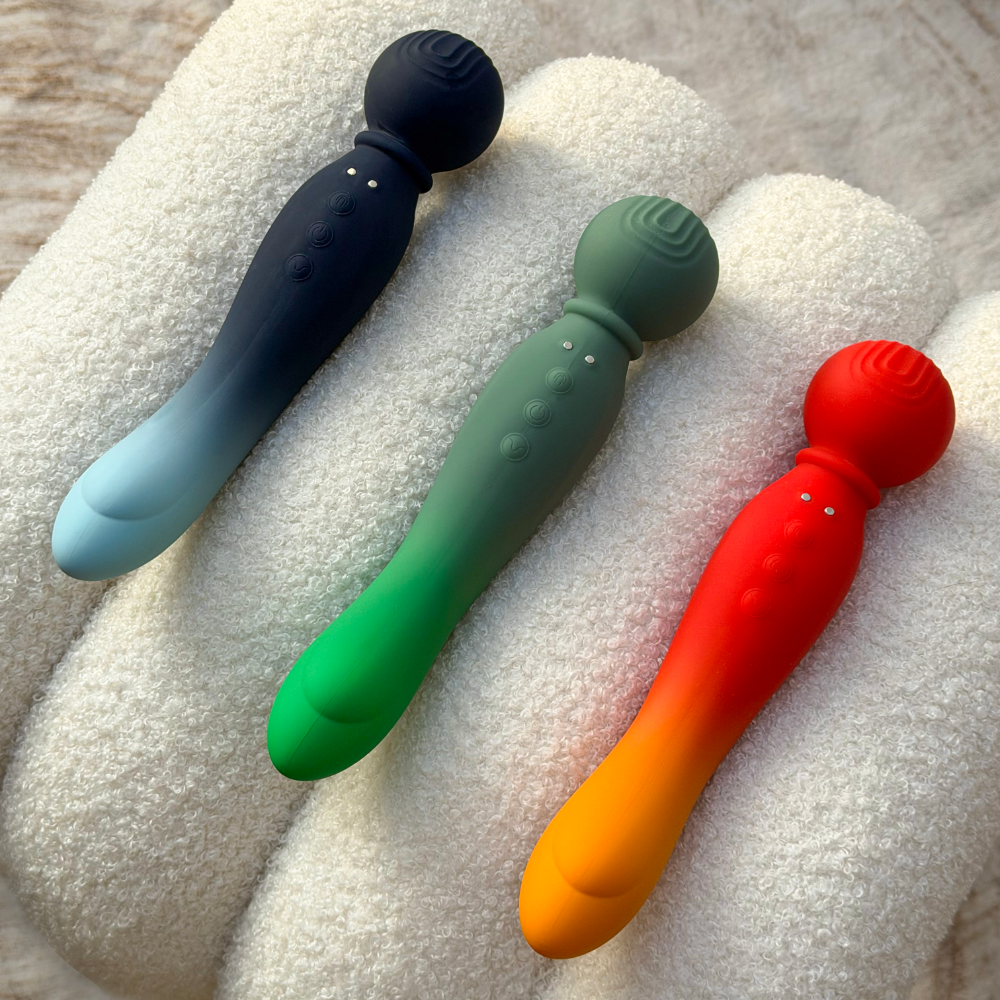 Three gradient-colored silicone vibrators with rounded heads and textured surfaces, displayed on a white towel.